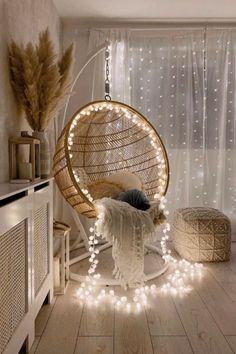 a hanging chair with lights around it in a room that has white curtains and wooden floors