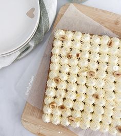 a square cake sitting on top of a wooden cutting board next to white plates and utensils