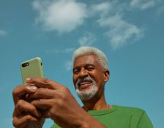 an older man taking a selfie with his cell phone in front of the sky