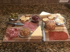 a wooden cutting board topped with cheese and meats next to crackers on a counter