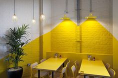 yellow tables and chairs are in front of a brick wall with three lamps on it