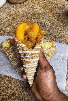 a hand holding an ice cream cone filled with fruit on top of a marble counter