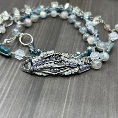 This incredible wrap bracelet has been a work in progress for a while. The combination of the pewter focal with the gorgeous 6mm flashy labradorite rounds absolutely enchanted me. From there, I added so many of my favorite things. In this bracelet, you’ll find apatite rectangles, the most insane faceted 8mm kyanite, 8mm starcut pale jade, flashy tourmilinated rainbow moonstone, smoky quartz, and the most incredible faceted prasiolite nuggets. Also featured are the prettiest faceted glass rondelles. Let’s circle back to the focal. The shape was so interesting and mysterious to me. I wrapped on faceted labradorite and iolite to bring out some of the lines. This wrap bracelet is sterling silver, with the exception of the USA made pewter focal. The knotted portion of the bracelet was done in h Silver Gemstone Beads Wrap Bracelet, Silver Gemstone Beads Wrap Bracelet As Gift, Silver Gemstone Beaded Wrap Bracelet As Gift, Silver Wrap Bracelet With Round Natural Stones, Silver Wrap Bracelet With Gemstone Beads For Gift, Silver Wrap Bracelet With Gemstone Beads, Silver Wrap Bracelet With Natural Stones, Silver Bohemian Multi-strand Wrap Bracelet, Silver Multi-strand Bracelet With Natural Stones