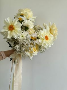 a bouquet of white and yellow flowers is tied to a wall with a beige ribbon