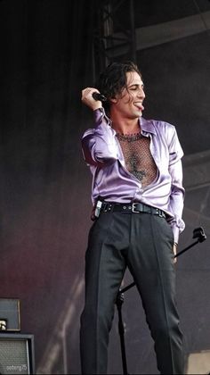 a man standing on top of a stage with his hands in the air while wearing a purple shirt and black pants