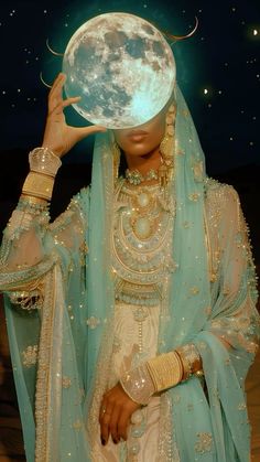 a woman in a blue and white dress holding up a large moon above her head