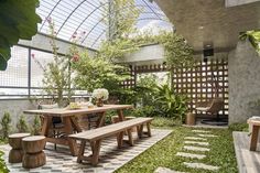 an outdoor dining area with wooden benches and tables in the center, surrounded by greenery