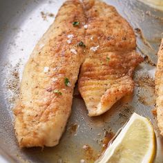 two pieces of fish are being cooked in a pan with lemon wedges on the side