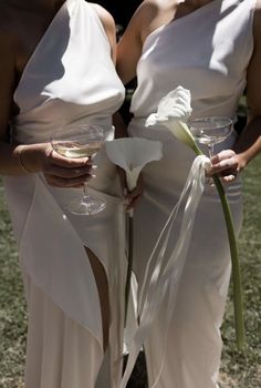 two women in white dresses holding wine glasses with flowers on the bottom and one wearing a flower