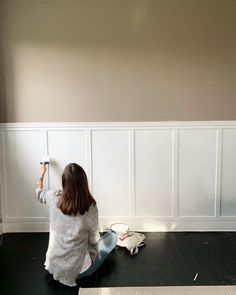 a woman sitting on the floor painting a wall