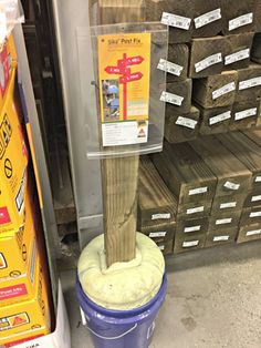 a blue bucket with a wooden post sticking out of it's side in front of stacks of boxes