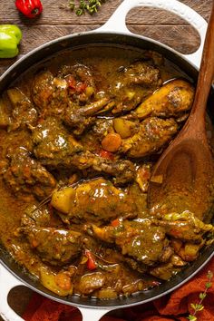 a pot filled with meat and vegetables on top of a wooden table next to peppers