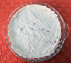 a cake with white frosting in a glass bowl on a red tableclothed surface