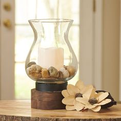 a glass vase filled with rocks and a lit candle on top of a wooden table