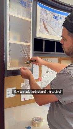 a man in grey shirt and black hat working on a cabinet with tape around it