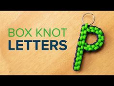 a green and black keychain sitting on top of a wooden table next to the words box knot letters