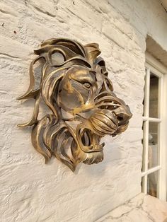 a metal lion head mounted to the side of a white brick wall next to a window