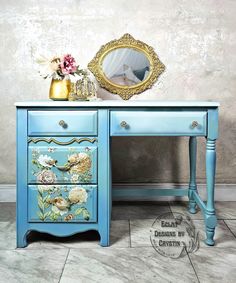 a blue painted desk with flowers and a gold mirror on it's top shelf