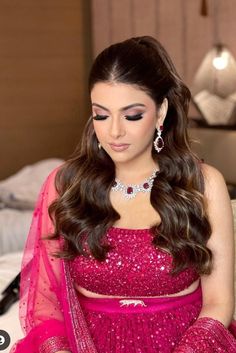 a woman in a pink dress sitting on a bed with long hair and wearing jewelry