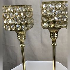 two gold colored candlesticks with clear crystal stones on them, sitting on a white surface