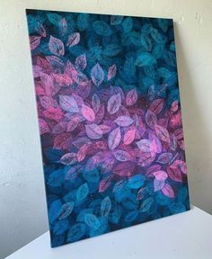 a painting with blue and pink leaves painted on it's canvas, against a white wall