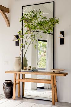 a wooden table topped with a mirror next to a vase filled with green plants and a potted plant