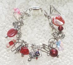 You'll sparkle with this one-of-a-kind charm bracelet.  Nineteen handcrafted charms in shades of red, pink, and silver silver dangle from handcrafted silver-tone links. Bracelet measures 7½" long and has a magnetic clasp for easy one-handed closure. Stock #7522-0123 Pink Charms, Pink Charm, Pink And Silver, Handcrafted Bracelets, Silver Charm Bracelet, Magnetic Clasp, Shades Of Red, Charm Bracelets, Silver Charms