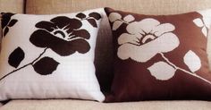 two brown and white pillows sitting on top of a beige couch next to each other