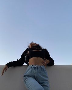 a woman laying on top of a white wall next to a sky background with her hands in her pockets