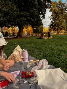 a woman sitting on top of a blanket next to a picnic table filled with food