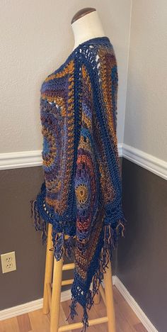 a crocheted shawl draped on top of a wooden stool next to a wall