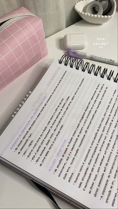 an open notebook sitting on top of a white desk next to a pink pencil holder