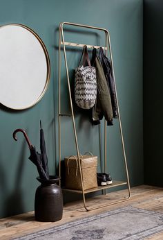 a coat rack with umbrellas and purses on it next to a round mirror