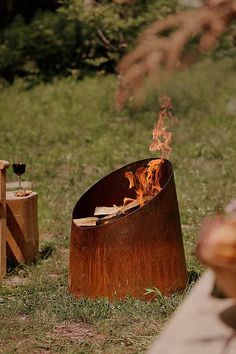 a fire pit sitting on top of a grass covered field next to two wooden stools