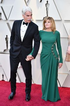 an older man and woman in formal wear walking down the red carpet at an oscars event