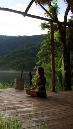 a woman sitting on a wooden deck in front of a body of water and trees