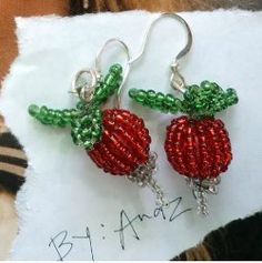 two strawberry shaped earrings on top of a piece of white paper with green beading