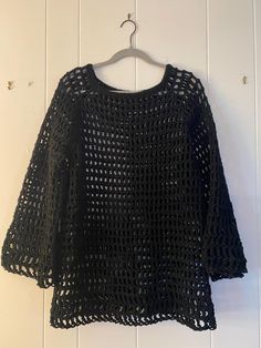 a black crochet sweater hanging on a white wall with a wooden hanger