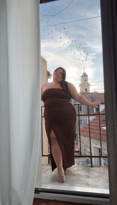 plus size woman stands on balcony in Split, Croatia wearing a brown curve-hugging maxi dress.