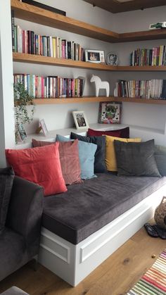 a couch with many pillows on it in front of a book shelf filled with books