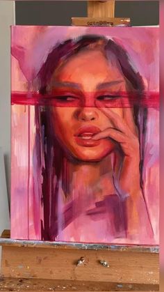 a painting on an easel with a woman's face painted in pink and purple