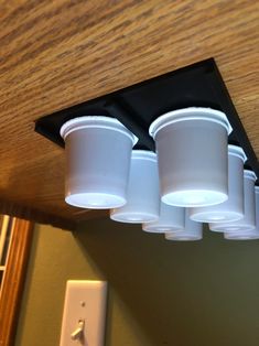 three white cups are hanging from the ceiling in front of an outlet for light bulbs