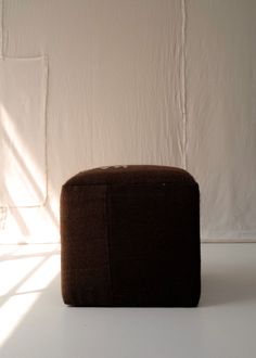 a brown ottoman sitting on top of a white floor next to a wall and window