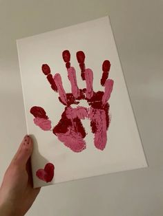 a person holding up a handprint with red paint on it in front of a white wall