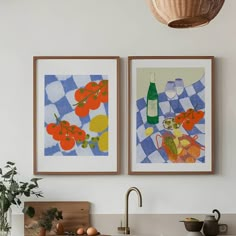 two paintings hanging above a kitchen sink next to a wooden cutting board with fruit and vegetables on it