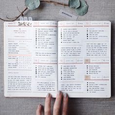 a hand is holding an open book next to a plant with leaves on the table