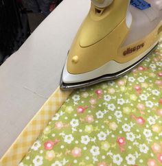 an iron is sitting on top of a table next to a piece of fabric with flowers