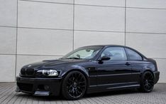 a black bmw is parked in front of a white wall and grey brick flooring