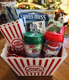 a basket filled with popcorn and snacks on top of a wooden table next to a christmas tree