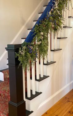 a set of stairs decorated with greenery and white pillar vases on each handrail